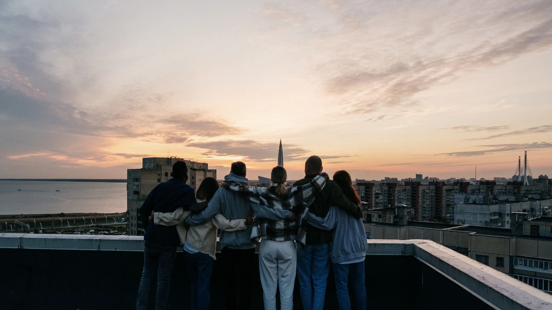 Siluetas de un grupo de amigos en una azotea al atardecer, con la ciudad debajo