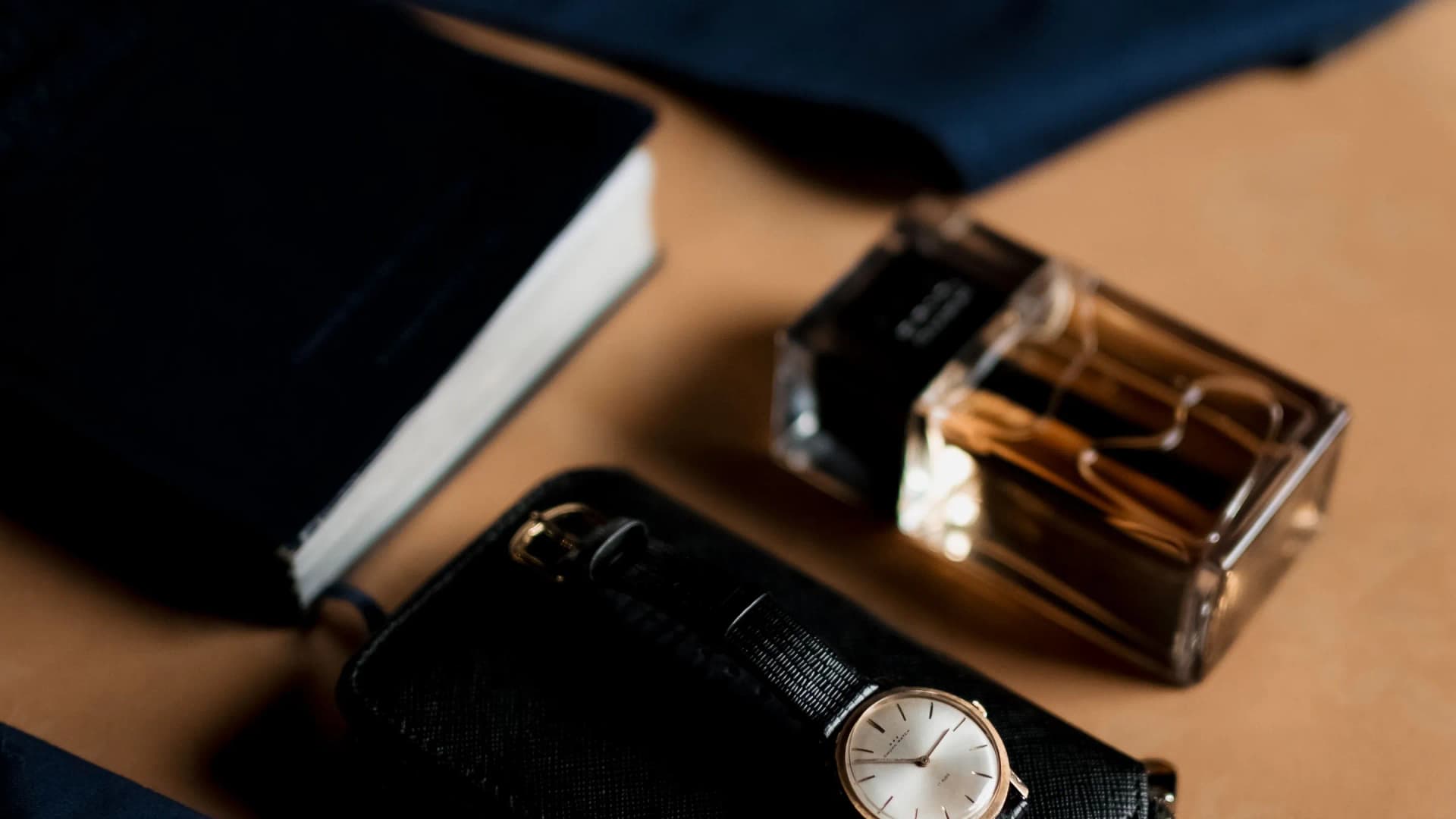 Un reloj sobre una cartera y un frasco de fragancia en una mesa