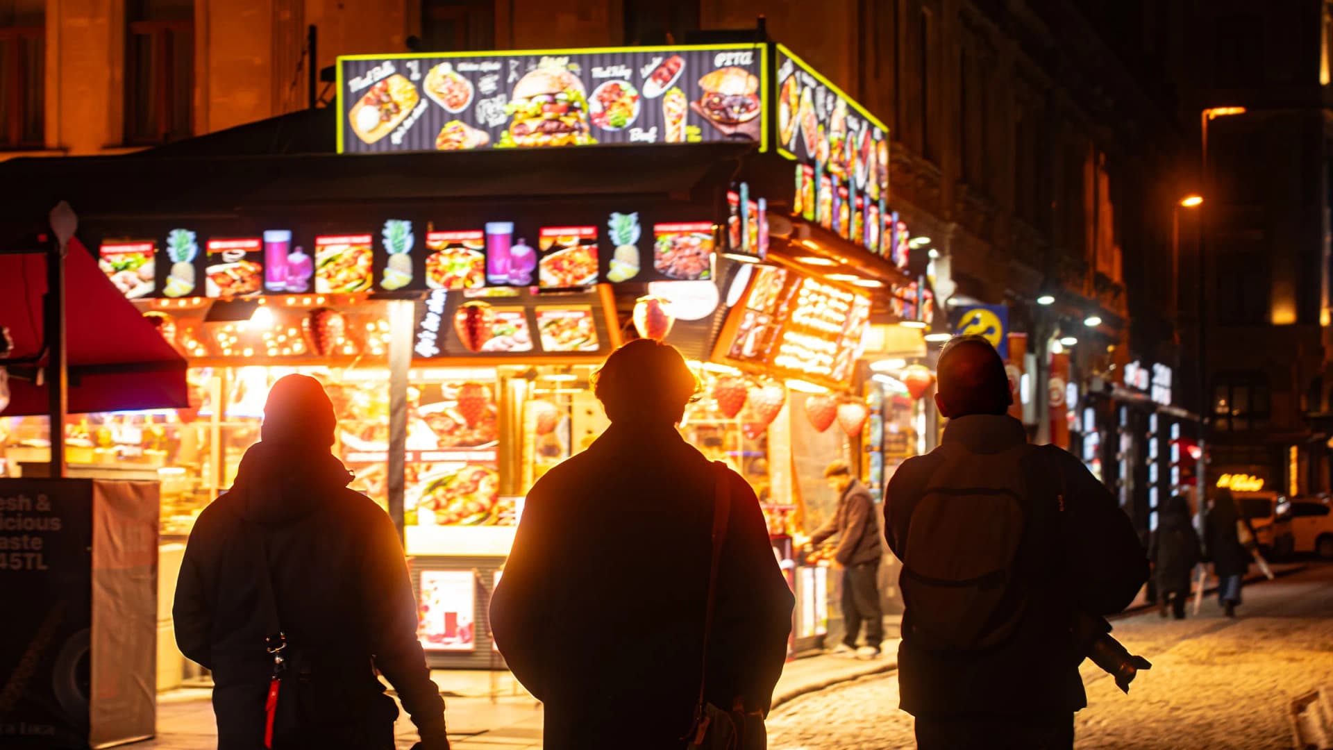 Personas frente a un local iluminado en una calle de noche