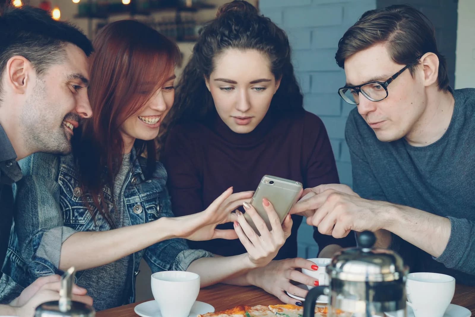 Cuatro amigos deciden un plan alrededor de un móvil en una mesa